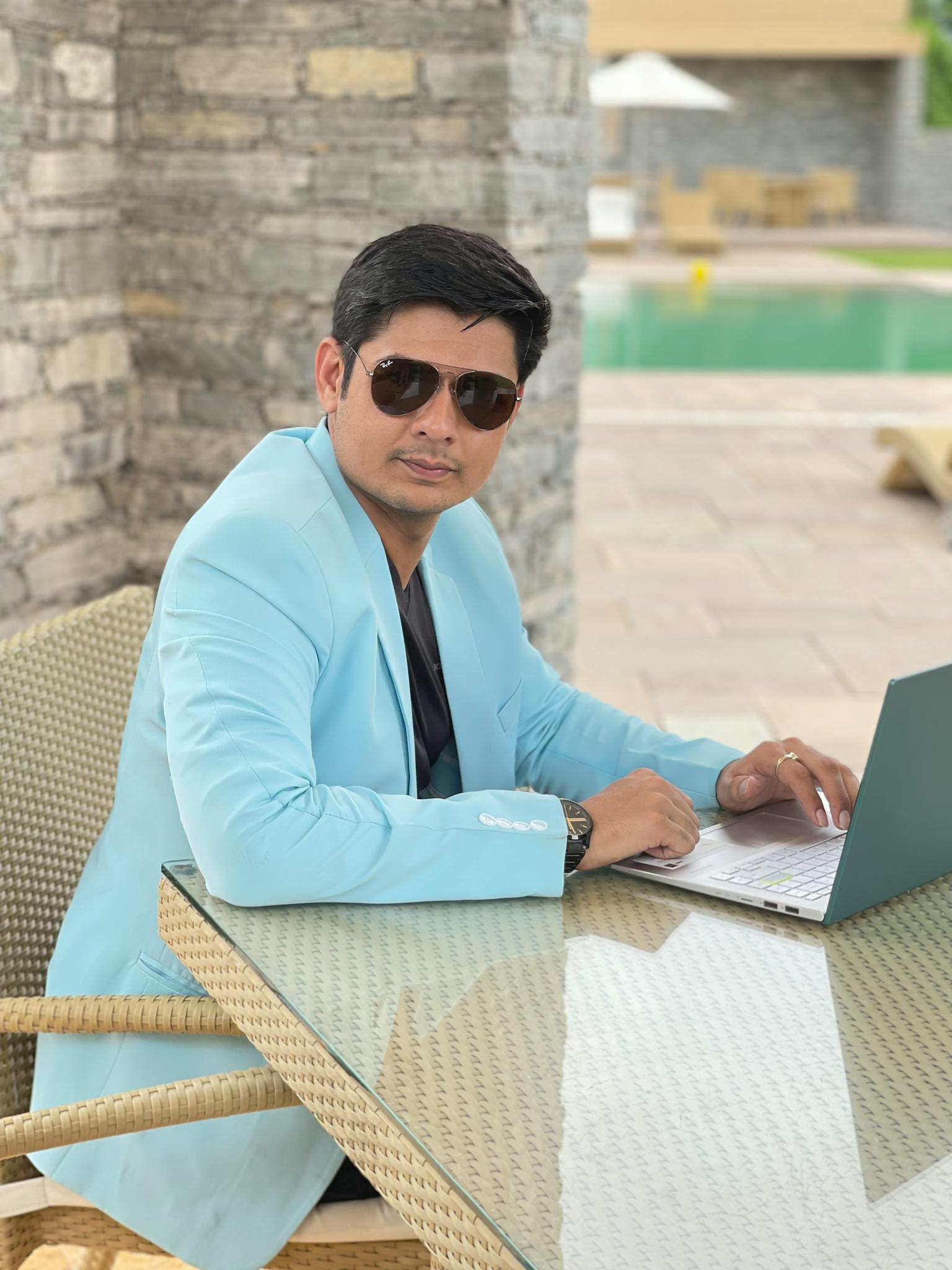 Stylish man with sunglasses using laptop outdoors by pool. Business concept.